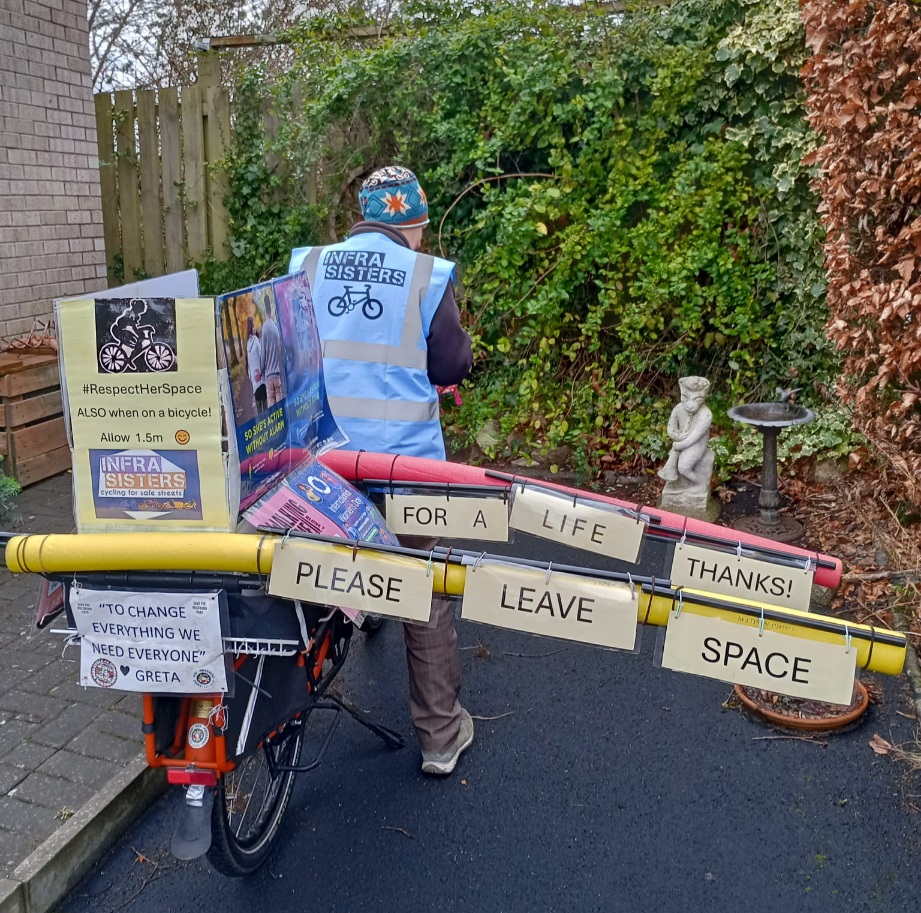 Someone on a big cargo bike wearing an InfraSisters tabard decorated with pool noodles to mark out 1.5m safe passing space